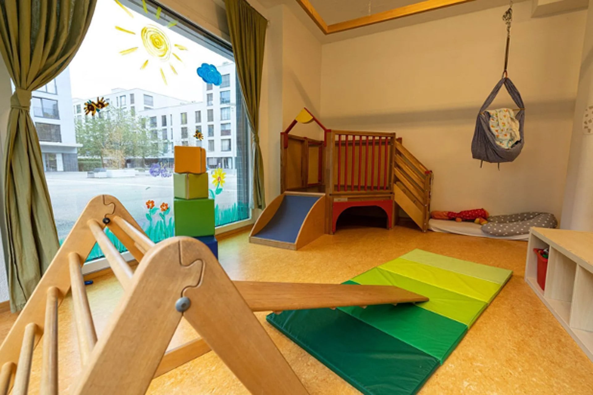 Kita kidsco Binzallee Bewegungsraum der Kita mit einer Fensterfront und Holzspielzeug und Holz Mobiliar